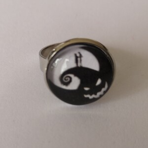 May include: A silver ring with a black and white round cameo featuring a silhouette of Jack Skellington from the Nightmare Before Christmas.