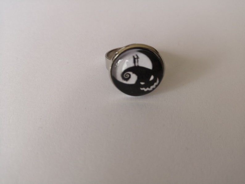 May include: A silver ring with a black and white round cameo featuring a silhouette of Jack Skellington from the Nightmare Before Christmas.