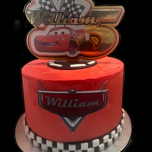May include: Red and white checkered cake with a red frosting and a Cars themed topper with the name William and a number 5.