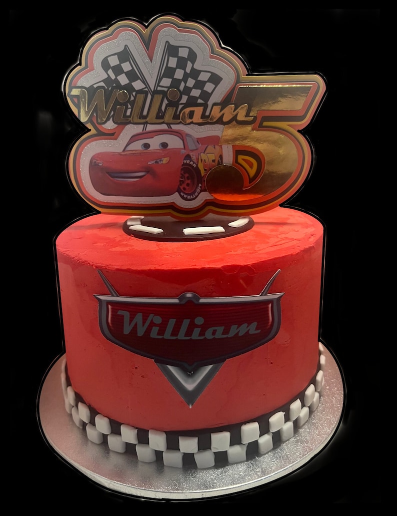 May include: Red and white checkered cake with a red frosting and a Cars themed topper with the name William and a number 5.