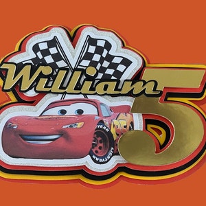 May include: A red race car with a smiling face, a gold number 5, and the name "William" in gold letters. The car is surrounded by checkered flags and a red, yellow, and black border.