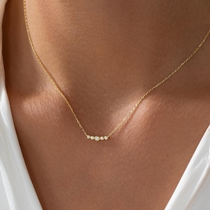 Op de afbeelding: Een delicate gouden ketting met een rij kleine, ronde diamanten in een gebogen lijn.
