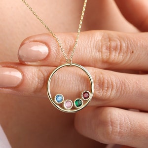 May include: A gold necklace with a circle pendant featuring four colorful gemstones. The gemstones are blue, pink, green, and red.