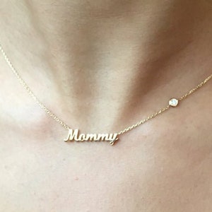 May include: A gold necklace with a delicate chain and a small diamond charm. The necklace features a pendant with the word "Mommy" in cursive script.