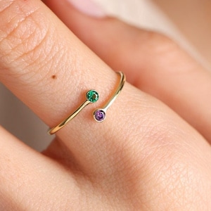 May include: A gold ring with a green and purple gemstone. The ring is designed to wrap around the finger.