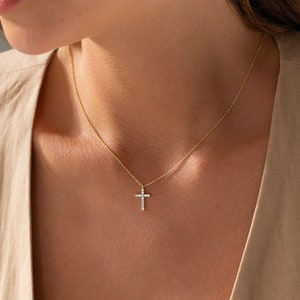 K&ouml;nnte beinhalten: Eine zarte goldene Kettenkette mit einem kleinen, funkelnden Diamantkreuz-Anh&auml;nger.