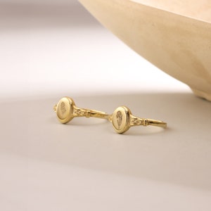 May include: Two gold rings with oval-shaped tops featuring a floral design. The rings are on a white surface.