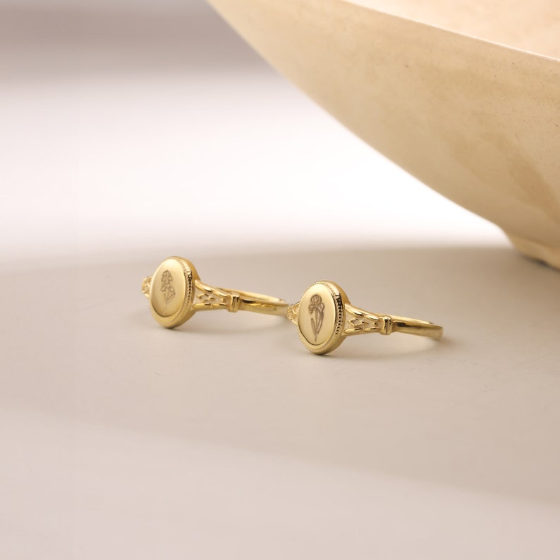 May include: Two gold rings with oval-shaped tops featuring a floral design. The rings are on a white surface.