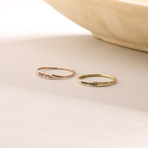 Puede incluir: Dos anillos de oro simples con delicados grabados florales. El anillo de la izquierda es de oro rosa y el anillo de la derecha es de oro amarillo.