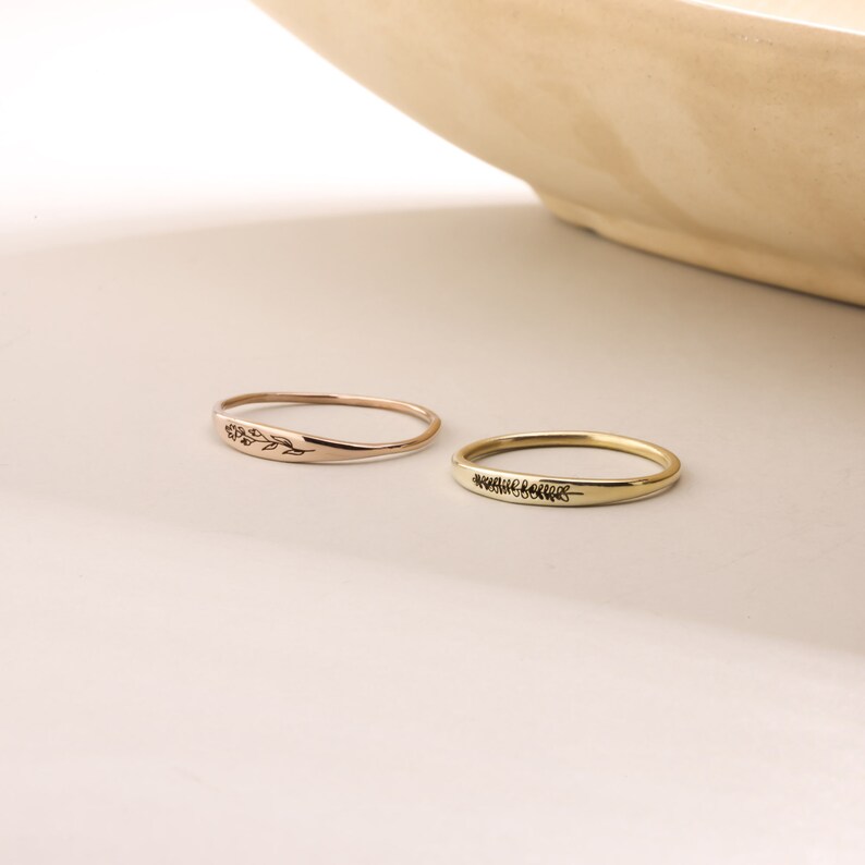 Puede incluir: Dos anillos de oro simples con delicados grabados florales. El anillo de la izquierda es de oro rosa y el anillo de la derecha es de oro amarillo.