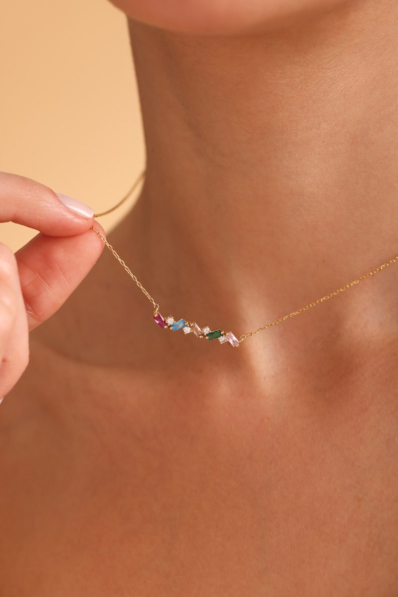 Puede incluir: Un collar de cadena de oro con una fila delicada de piedras preciosas de colores. Las piedras preciosas son de diversas formas y tama&ntilde;os, incluyendo baguette, redonda y ovalada. El collar es una pieza de joyer&iacute;a hermosa y &uacute;nica.
