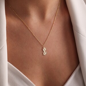 May include: A gold necklace with a delicate pendant featuring a cluster of small leaves. The pendant is a simple and elegant design.