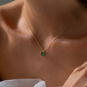 May include: A delicate gold chain necklace with a small emerald green gemstone pendant.