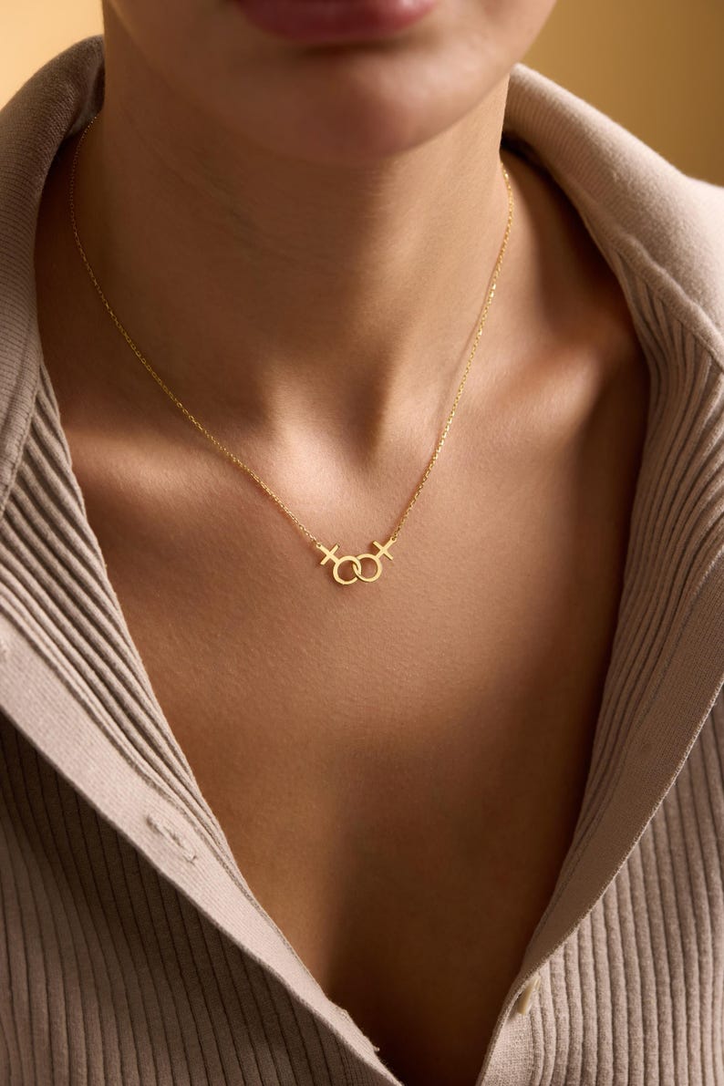 May include: A gold necklace with a delicate chain and a pendant featuring two interlocking circles with a small cross on each side.