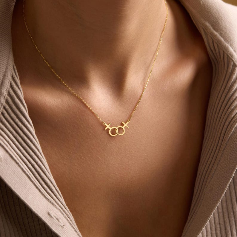 May include: A gold necklace with a delicate chain and a pendant featuring two interlocking circles with a cross on each side.