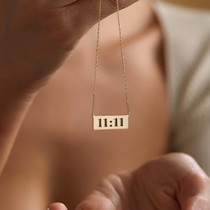 K&ouml;nnte beinhalten: Eine goldene Kettenkette mit einem rechteckigen Anh&auml;nger, auf dem in Schwarz "11:11" steht.