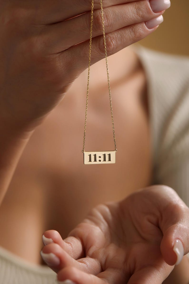 K&ouml;nnte beinhalten: Eine goldene Kettenkette mit einem rechteckigen Anh&auml;nger, auf dem in Schwarz "11:11" steht.