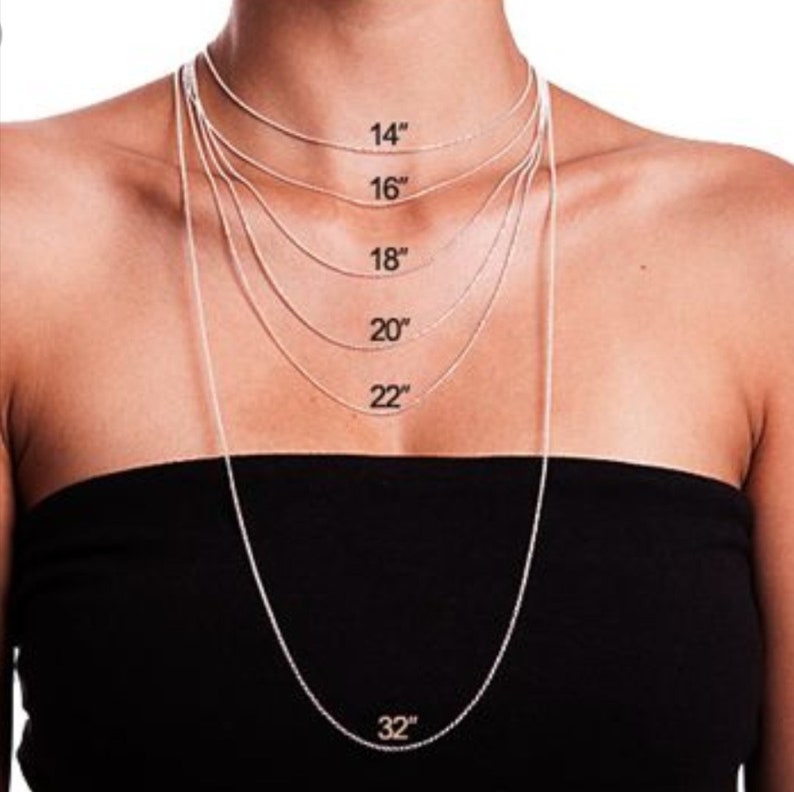 Puede incluir: Una modelo lleva un collar de cadena de plata en varias longitudes, de 35,56 cm a 81,28 cm. El collar se muestra en una persona con una blusa negra.
