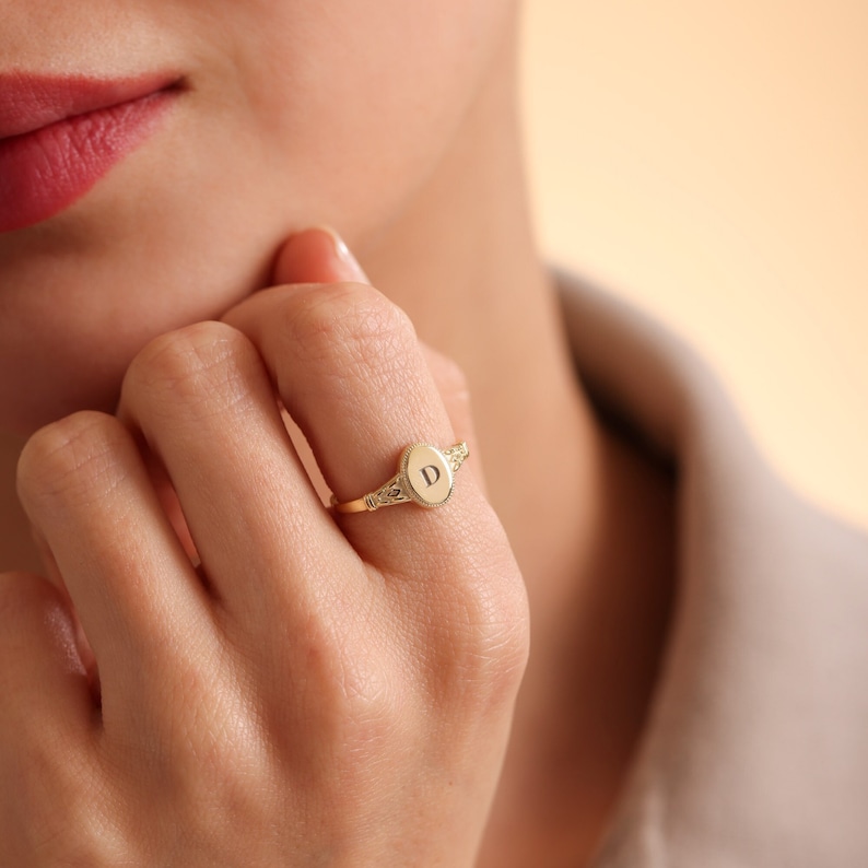 May include: A gold signet ring with an oval-shaped top featuring the letter "D" engraved on it.
