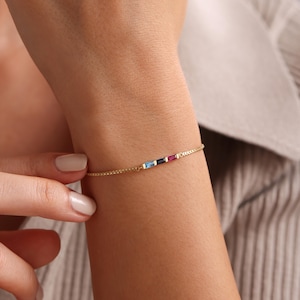 May include: A gold chain bracelet with a row of colorful gemstones. The gemstones are blue, dark blue, red, and yellow.