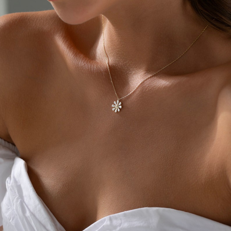 May include: A delicate gold chain necklace with a small white daisy pendant.