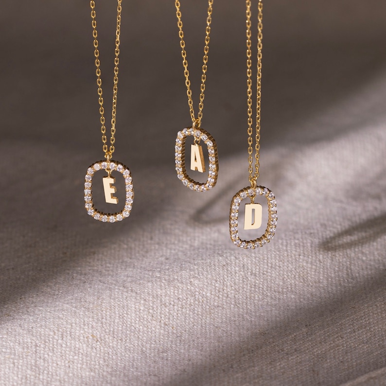 K&ouml;nnte beinhalten: Drei goldene Halsketten mit diamantbesetzten Anh&auml;ngern mit den Buchstaben A, D und E.