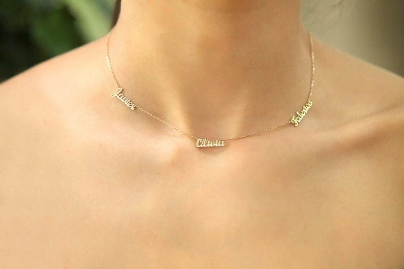 May include: A gold necklace with three names on it: "Lauren", "Olivia", and "Fabiana".