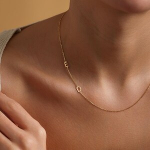 May include: A delicate gold chain necklace with two small, initial charms. The charms are the letters "E" and "D".