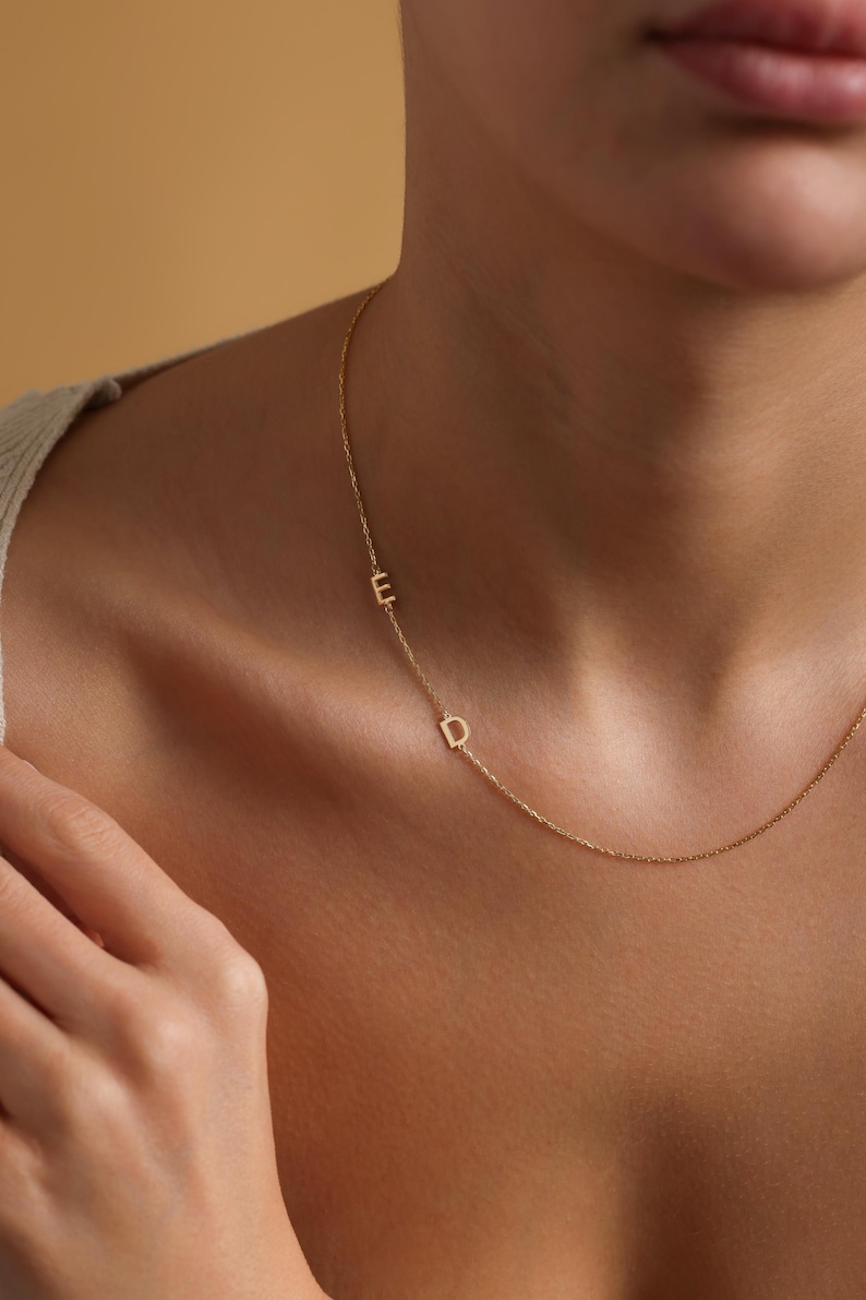 May include: A delicate gold chain necklace with two small, initial charms. The charms are the letters "E" and "D".
