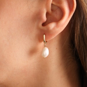 May include: Gold hoop earrings with a single white pearl dangling from each hoop.