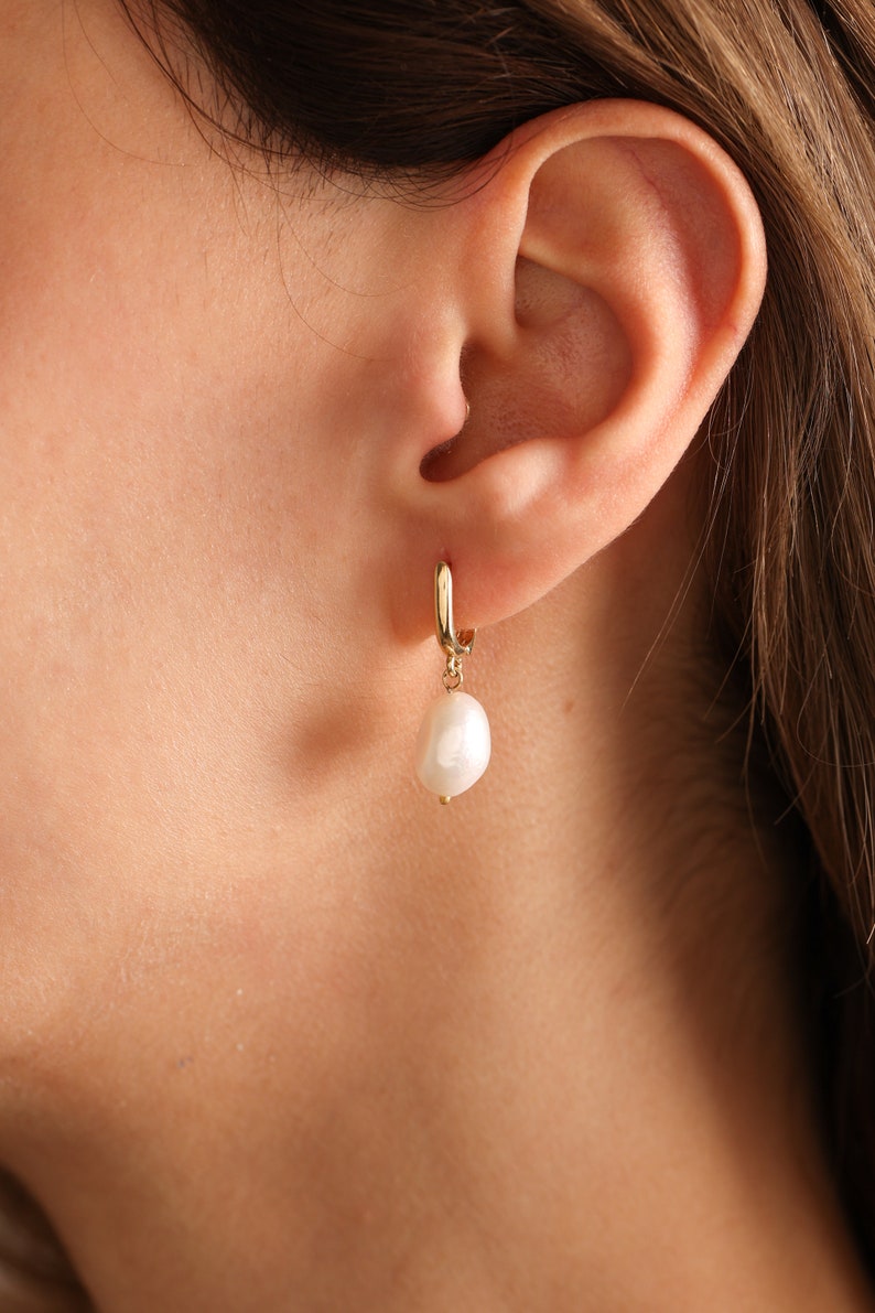 May include: Gold hoop earrings with a single white pearl dangling from each hoop.