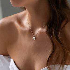 May include: A delicate gold chain necklace with a small white daisy pendant.