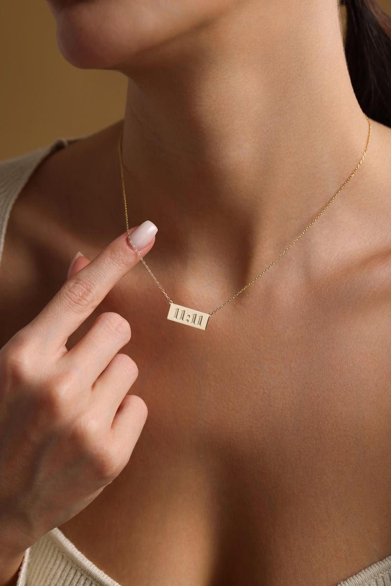 K&ouml;nnte beinhalten: Eine goldene Halskette mit einem rechteckigen Anh&auml;nger, auf dem in einer minimalistischen Schrift "11:11" steht.