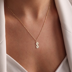 May include: A gold chain necklace with a small pendant featuring a cluster of stylized leaves.