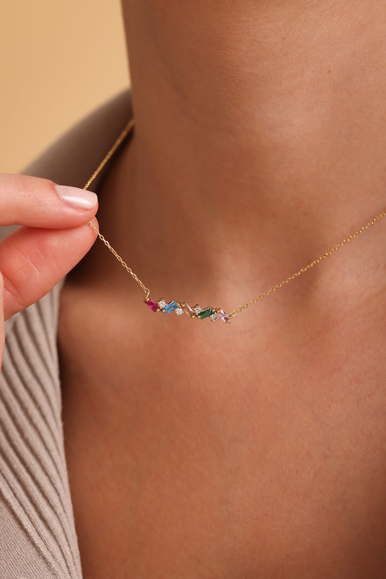 Puede incluir: Un collar de cadena de oro con una fila delicada de piedras preciosas de colores. Las piedras preciosas son de diversas formas y tama&ntilde;os, incluyendo esmeralda, zafiro, rub&iacute; y topacio.