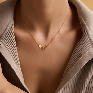 May include: A gold chain necklace with a pendant featuring interlocking symbols of the male and female genders.