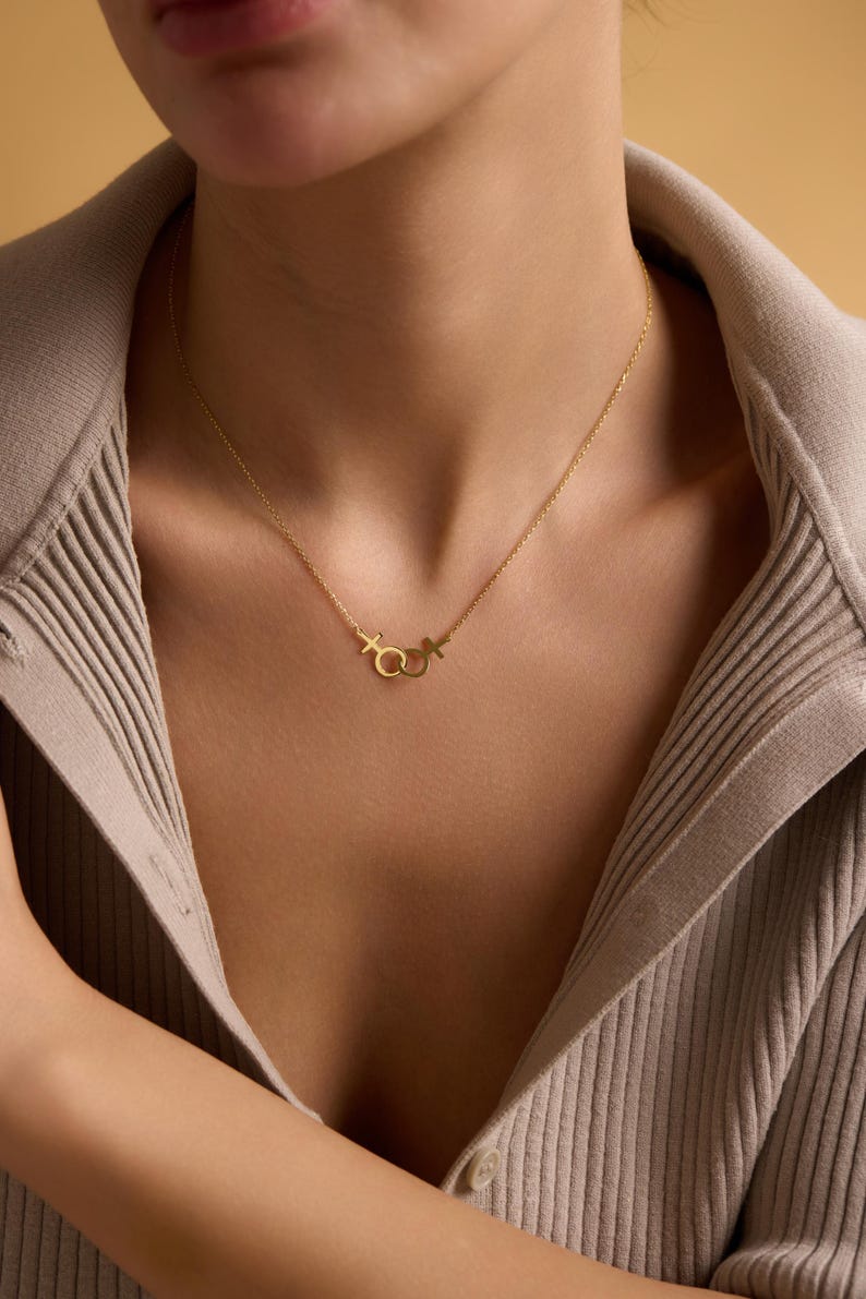 May include: A gold chain necklace with a pendant featuring interlocking symbols of the male and female genders.
