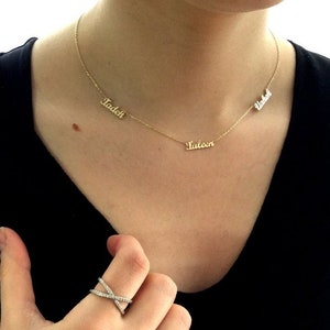 May include: A gold necklace with three nameplates: "Tadeh", "Taleen", and "Vahe" hanging on a person's neck.