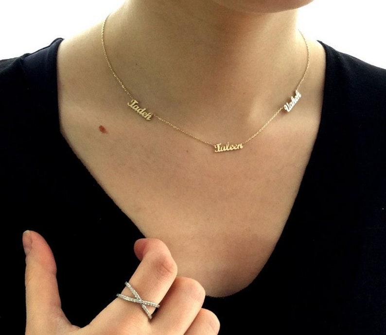 May include: A gold necklace with three nameplates: "Tadeh", "Taleen", and "Vahe" hanging on a person's neck.