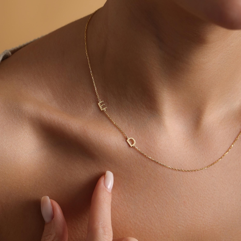 May include: A delicate gold chain necklace with two small, letter charms. The charms are the letters "E" and "D".