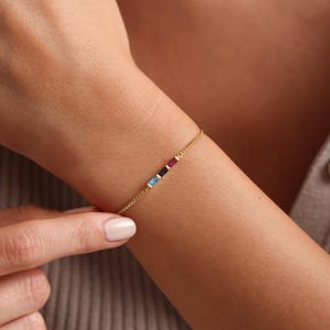 May include: A gold chain bracelet with four small, rectangular gemstones in blue, blue, black, and red.
