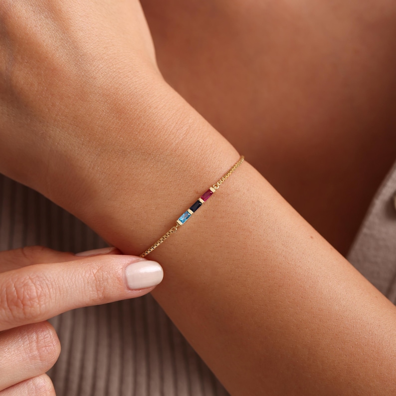May include: A gold chain bracelet with four small, rectangular gemstones in blue, blue, black, and red.