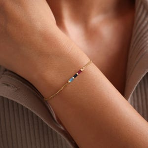 May include: A gold chain bracelet with four small, colorful gemstones. The gemstones are blue, dark blue, red, and yellow.
