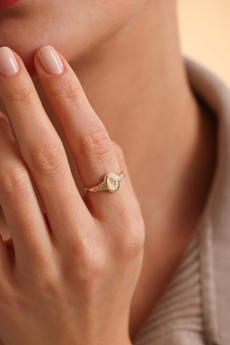 May include: A gold signet ring with an oval-shaped top featuring a floral design.