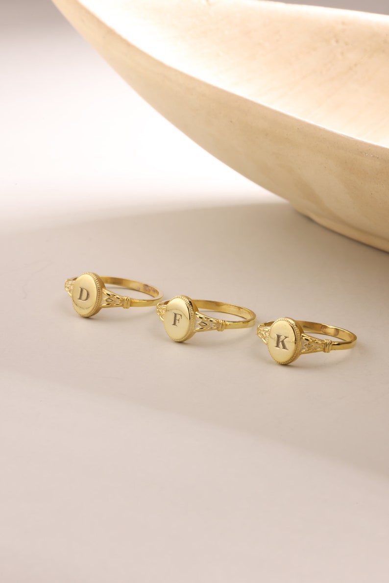 May include: Three gold rings with oval-shaped tops. The tops are engraved with the letters D, F, and K.