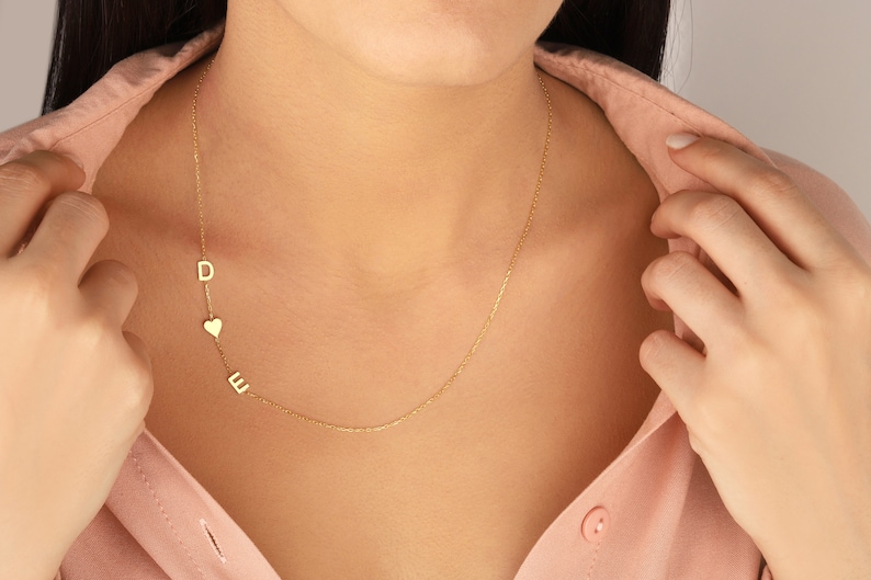 May include: A gold chain necklace with a heart charm and two letter charms, D and E.