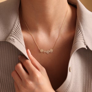 K&ouml;nnte beinhalten: Eine goldene Halskette mit einer zarten Kette und einem Anh&auml;nger mit drei miteinander verbundenen Blumenmotiven.