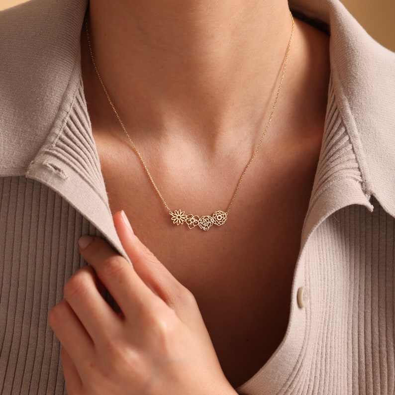 K&ouml;nnte beinhalten: Eine goldene Halskette mit einer zarten Kette und einem Anh&auml;nger mit drei miteinander verbundenen Blumenmotiven.