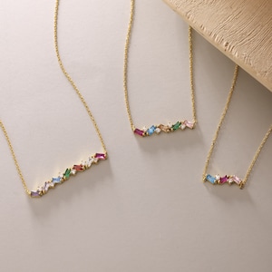 Puede incluir: Tres collares de oro con detalles de piedras preciosas de colores. Cada collar presenta una fila de peque&ntilde;as piedras preciosas rectangulares de varios colores, incluyendo rosa, azul, verde y rojo. Las piedras preciosas est&aacute;n engastadas en una cadena de oro.