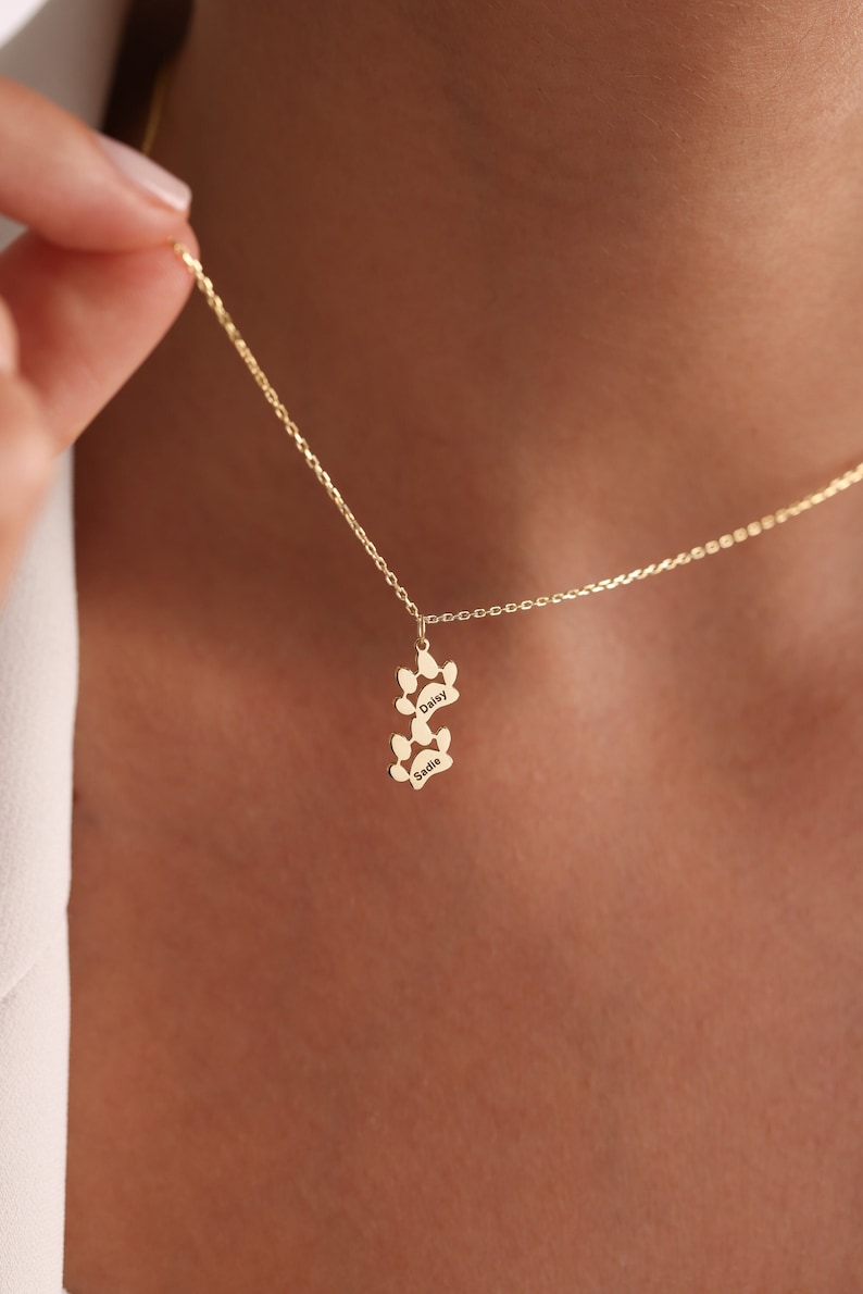 May include: Gold necklace with two paw print charms, each engraved with a dog's name: Daisy and Sadie.